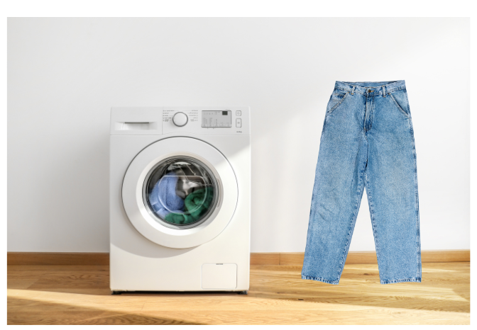 Front-loading washing machine with upright blue jeans beside it on a wooden floor.