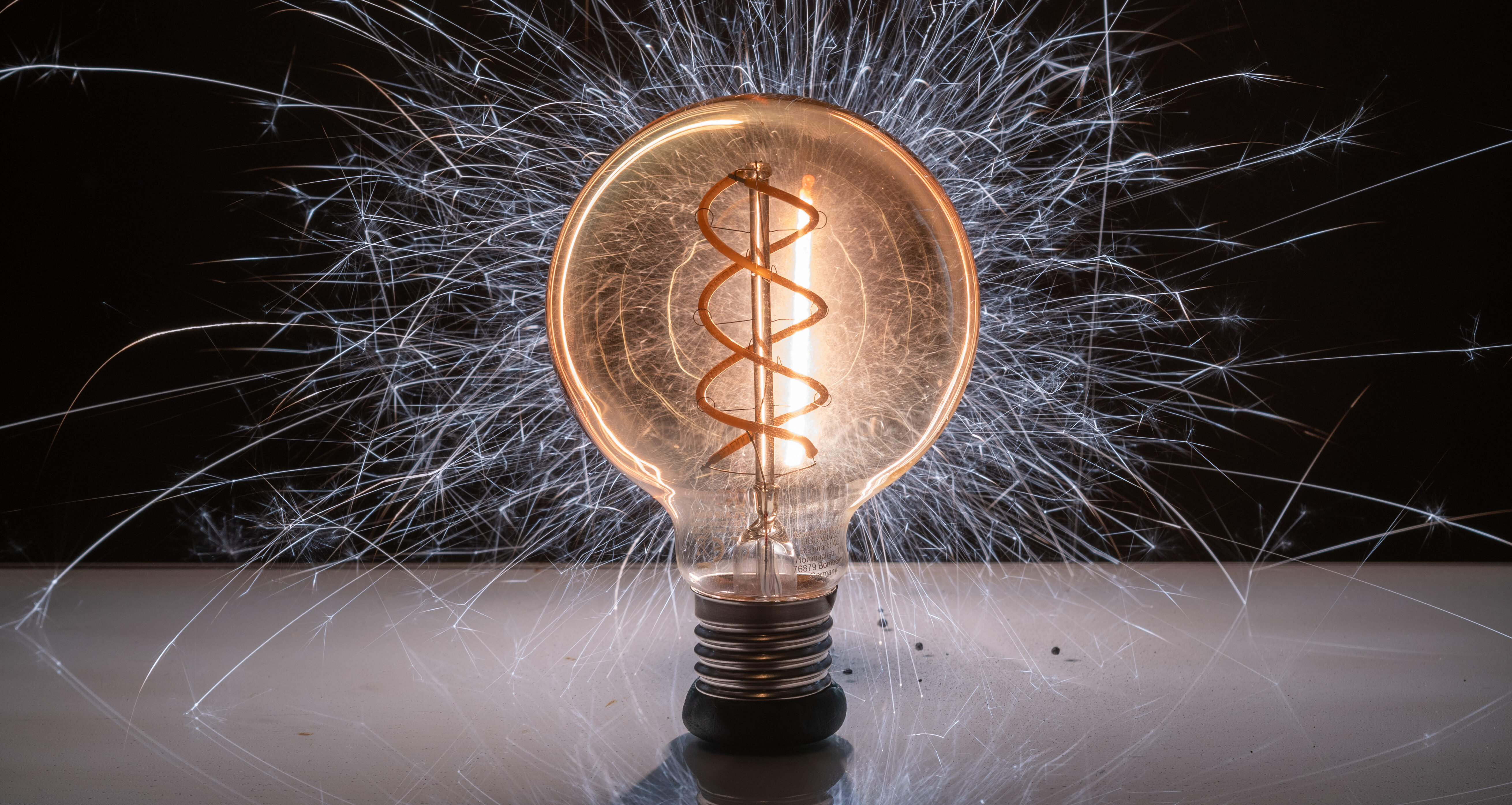 Glowing light bulb with sparks against a dark background.