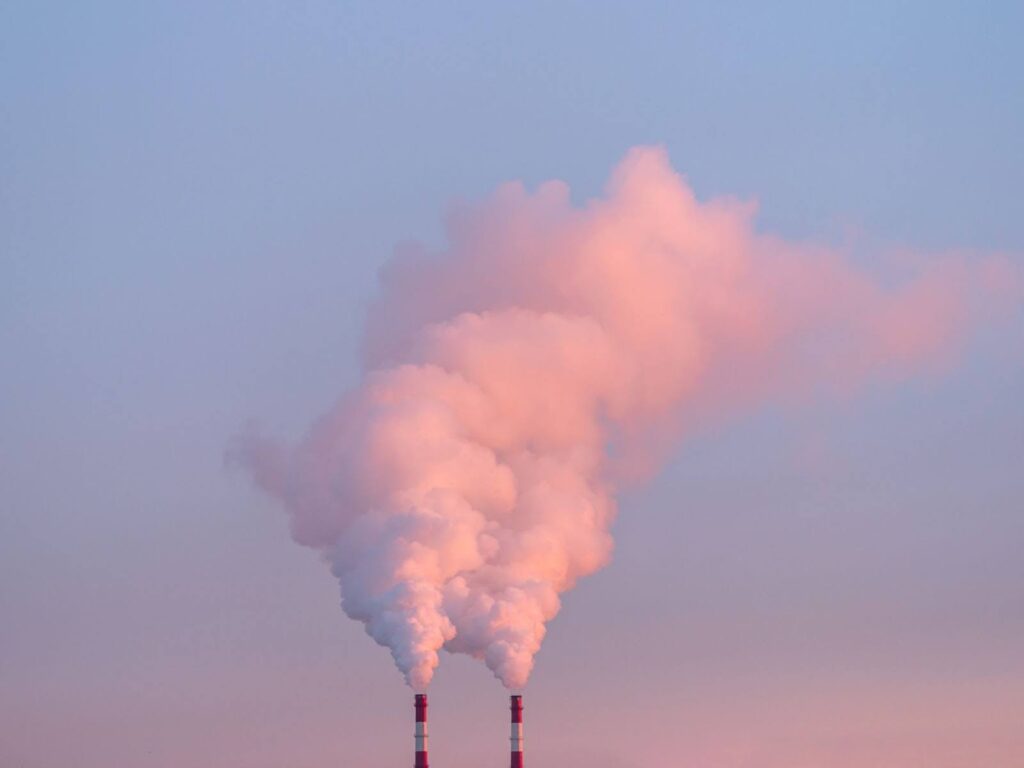 Two chimneys emitting white smoke against a blue sky.