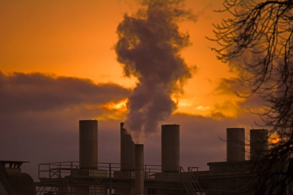 Factory smokestack releasing dark smoke at sunset.
