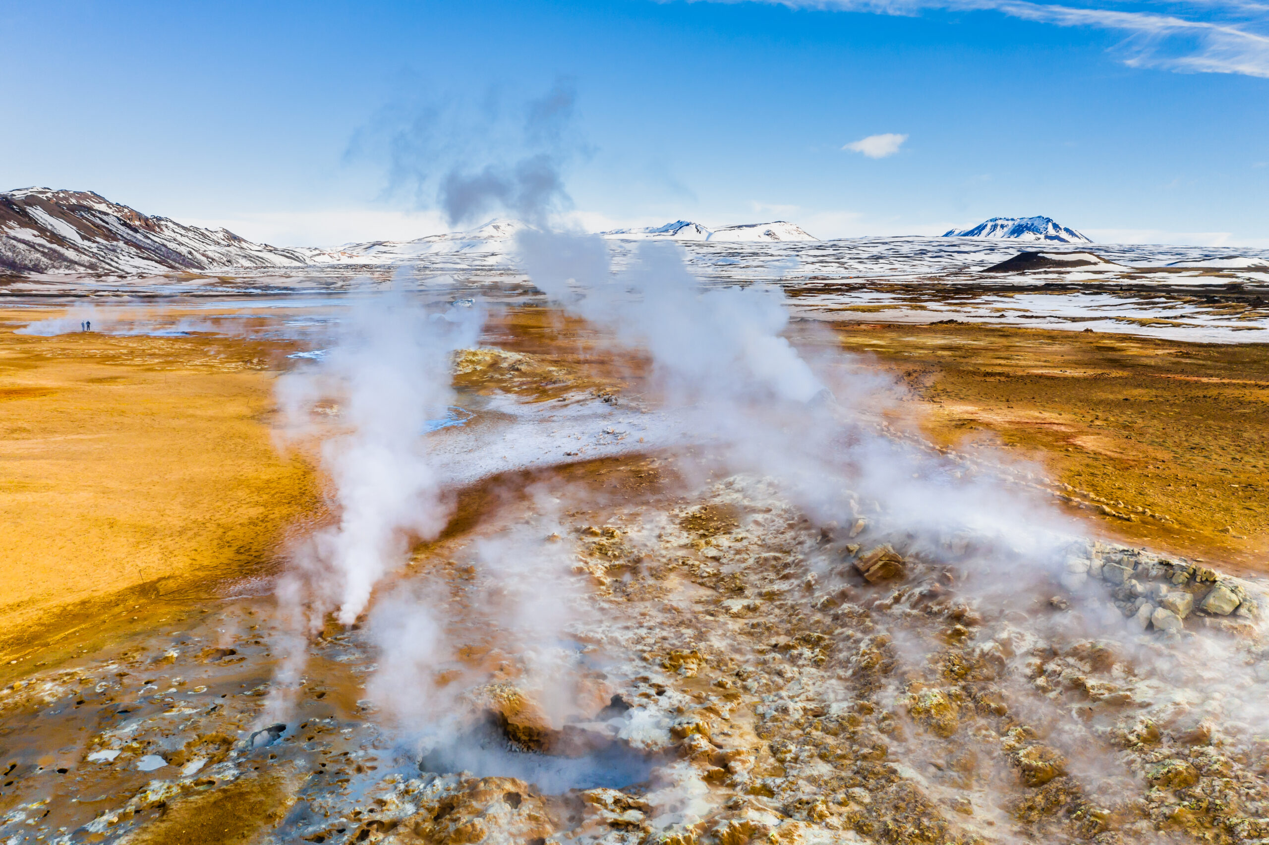 Aerial view of steaming geothermal vents across a snowy, barren plain.