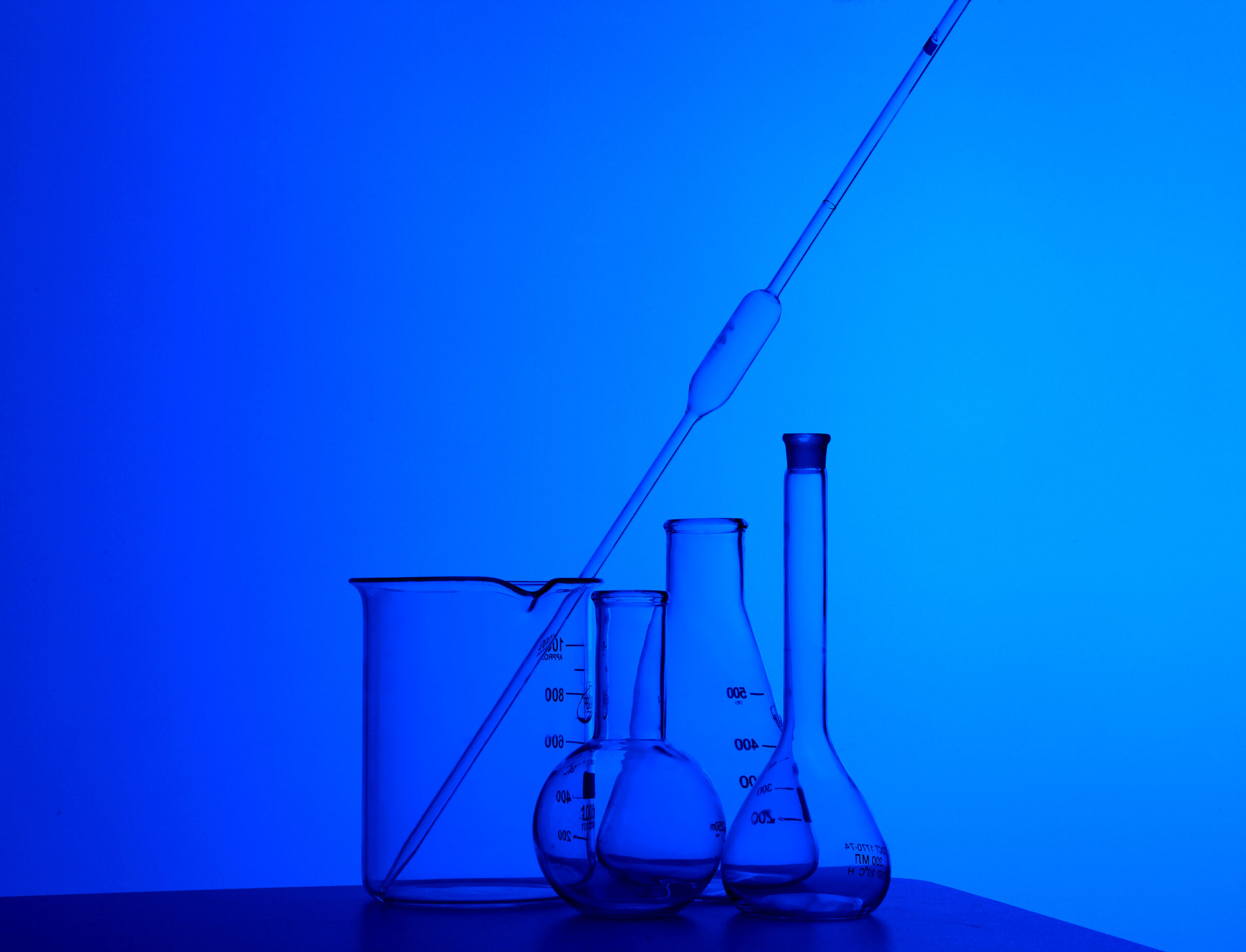 Chemistry measuring beakers and glass tubes, illuminated by blue light.